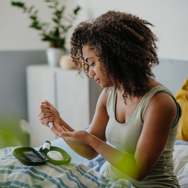 Woman sitting on bed testing blood sugar